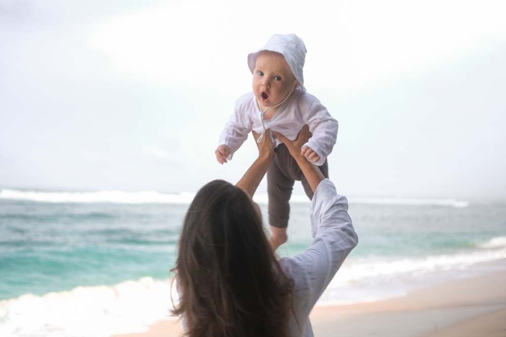 Young woman holding up baby on beach